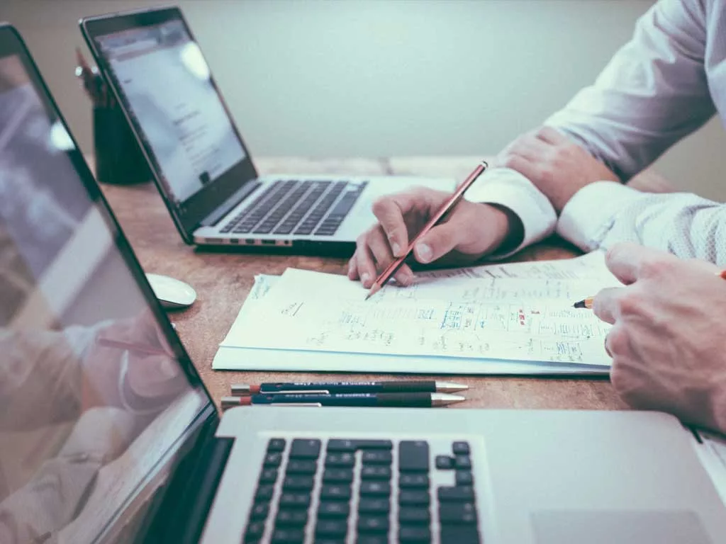 Twee mensen werken samen aan laptops en papieren.